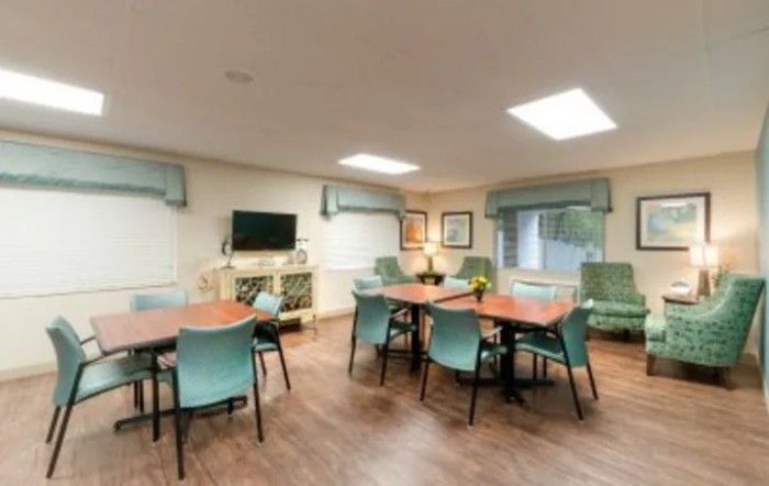 A well-lit meeting room with tables, chairs, and a television.