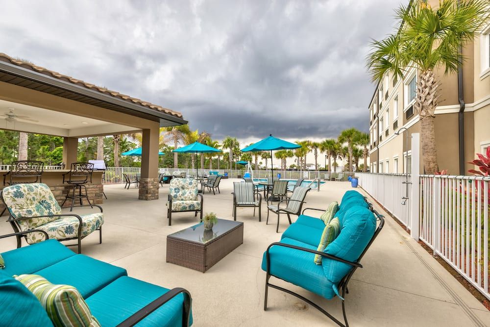 A relaxing patio area with teal cushioned chairs and umbrellas under a cloudy sky.