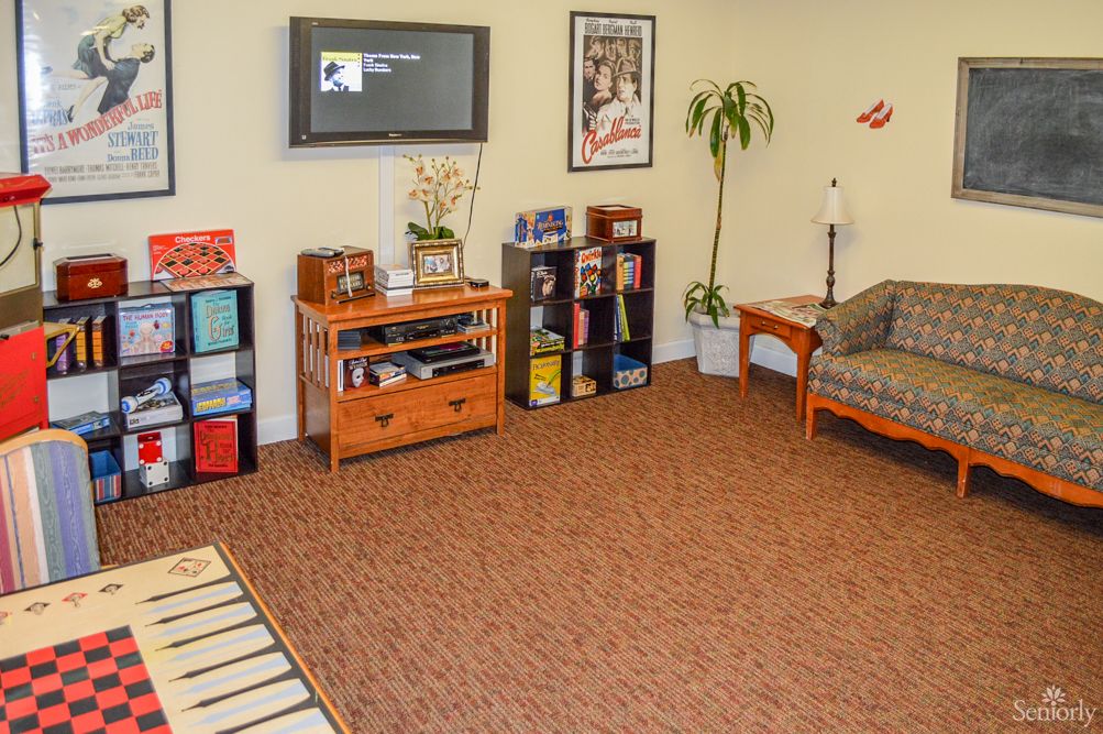A cozy waiting room with seating, a television, bookshelves, and decorative plants.