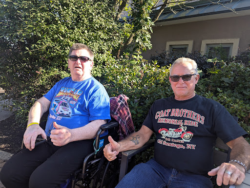 Two friends enjoying a sunny day outdoors, both giving a thumbs up.