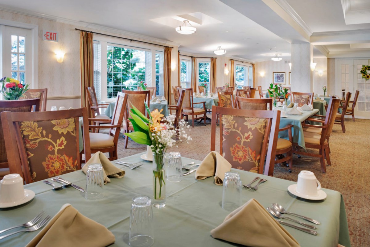 An elegantly set dining room with neatly arranged tables, flowers, and large windows providing natural light.