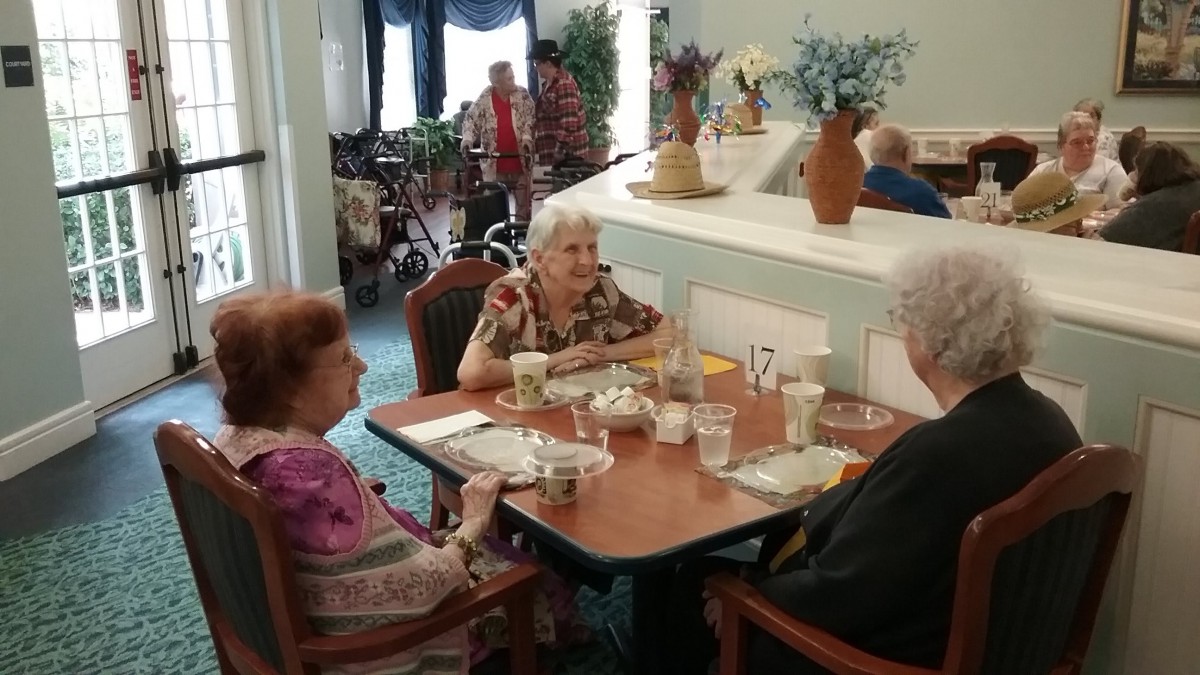 A group of elderly individuals sitting at a dining table, engaging in conversation over a meal in a communal setting.
