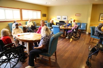 A nursing home community room with seniors engaging in conversation and activities.