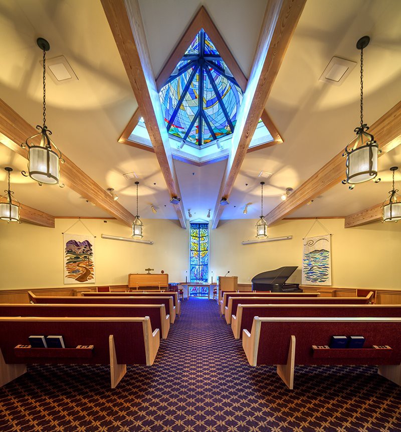 A beautifully designed chapel interior featuring wooden pews, stained glass windows, and elegant lighting fixtures.