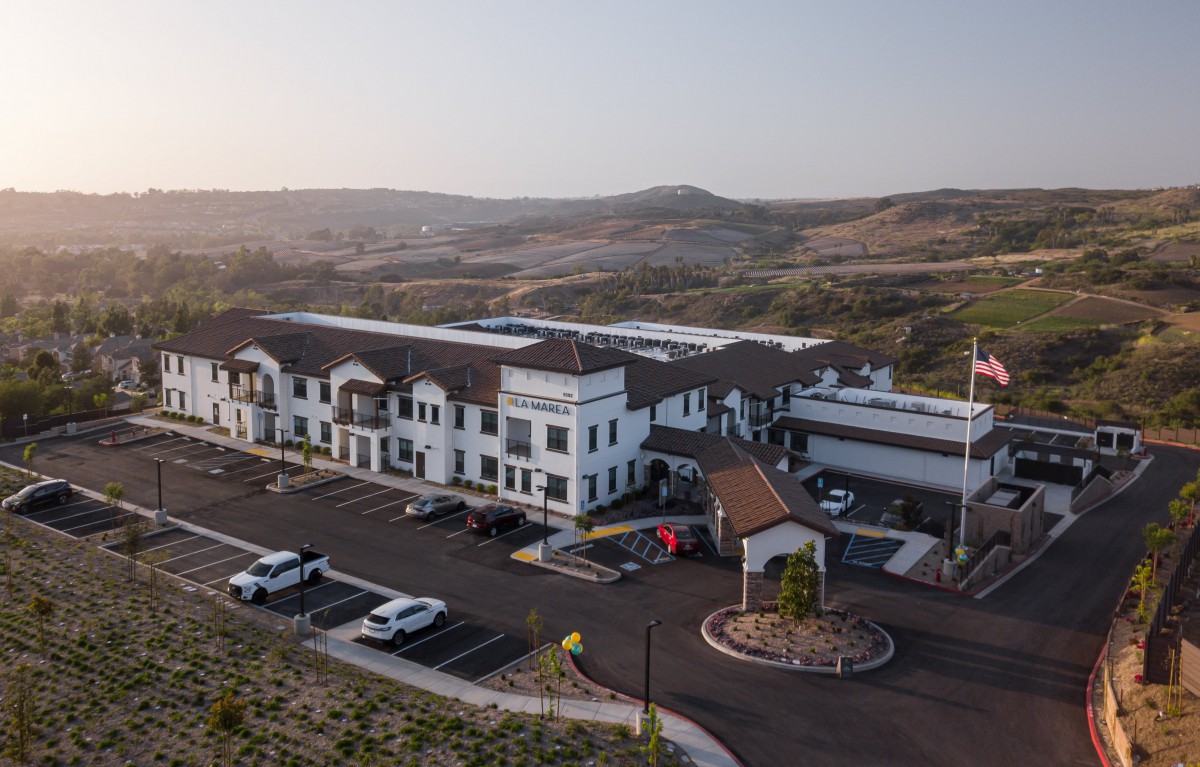 Aerial view of a large building with a parking lot, set against rolling hills.