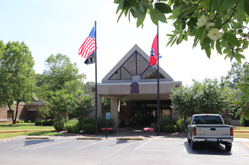 The entrance of a building adorned with the American and Tennessee flags, surrounded by greenery.