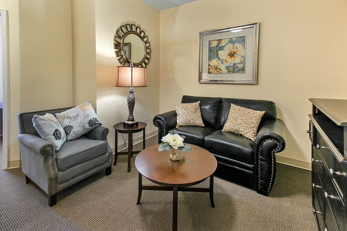 A cozy living room with a leather sofa, armchair, coffee table, and decorative elements like a lamp, mirror, and artwork.