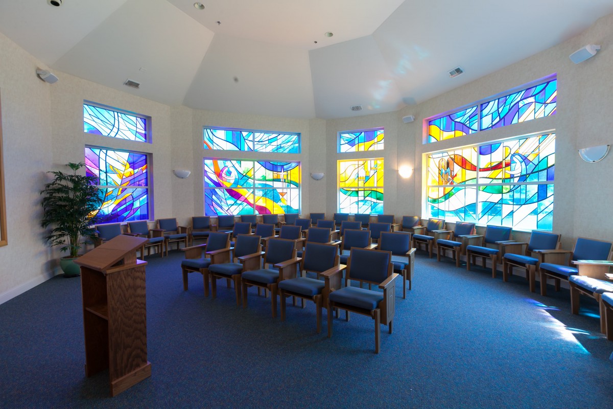 A serene chapel interior featuring vibrant stained glass windows and neatly arranged seating.
