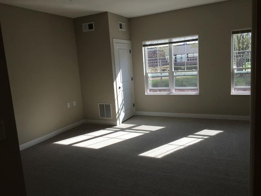 An empty room with sunlight streaming through a window onto the carpeted floor.