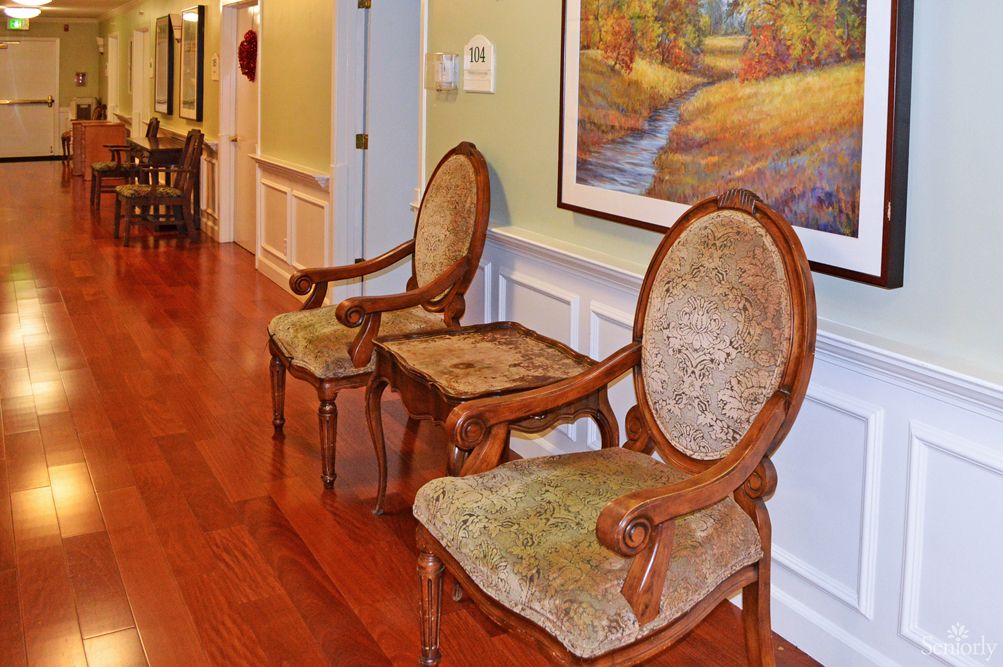 A pair of classic upholstered chairs in a hallway with wooden flooring and a landscape painting on the wall.