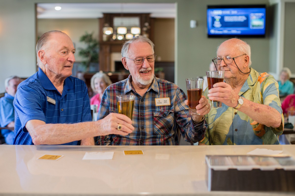 Three elderly men enjoying drinks and toasting at a bar.