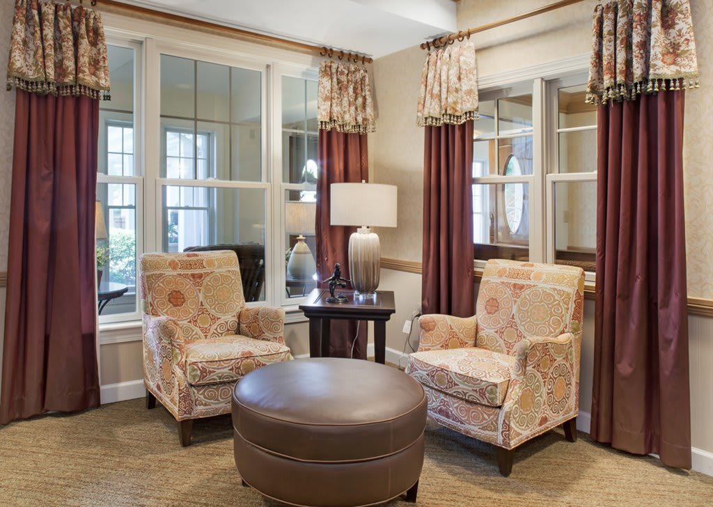 A cozy living room setting with two armchairs, a round coffee table, and a lamp by large windows adorned with curtains.