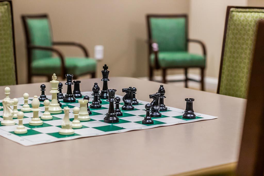 Chess game set up in a cozy room with chairs in the background.
