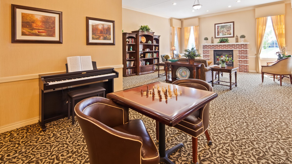 A cozy living room featuring a chess board, piano, and bookshelves.