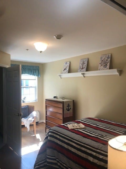 A neatly arranged bedroom with a bed, dresser, and chair by a window.