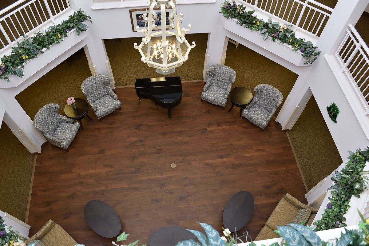 An elegant interior with a central grand piano surrounded by comfortable seating and a large chandelier overhead.