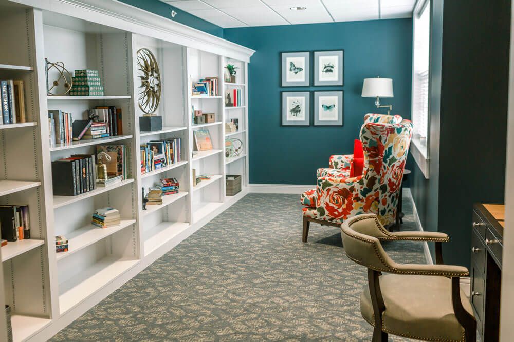 A cozy library corner featuring built-in bookshelves, colorful armchairs, and decorative wall art.