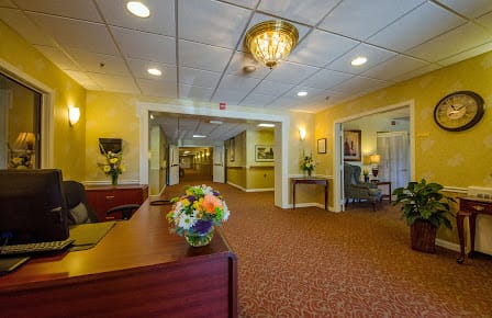 A well-decorated lobby area featuring a reception desk, floral arrangements, and a chandelier.