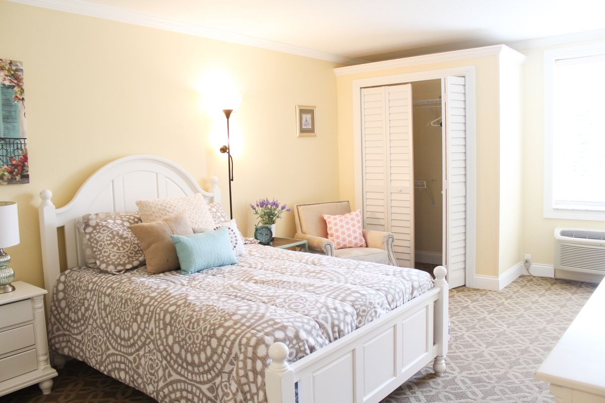 A cozy bedroom featuring a bed with neutral-colored bedding, a standing lamp, and soft lighting.