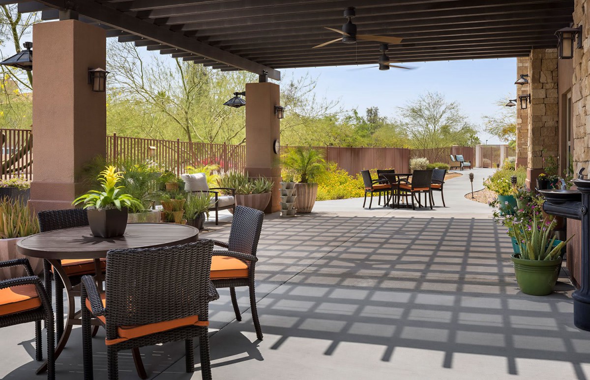 An outdoor patio area with comfortable furniture under a pergola, surrounded by lush garden landscaping.