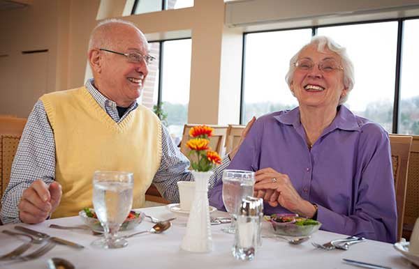 An elderly couple enjoying a meal together at a restaurant, sharing smiles and laughter.