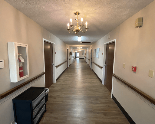 A long hallway with wooden floors, featuring multiple doors and a chandelier hanging from the ceiling.