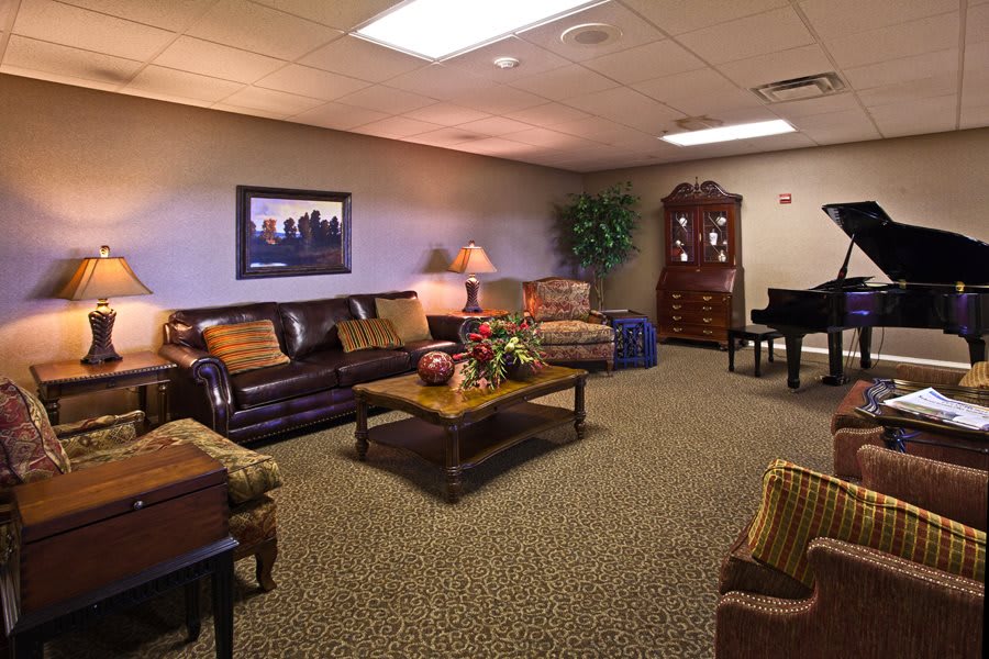 A cozy living room with a leather sofa, coffee table, and piano, decorated with artwork and plants.