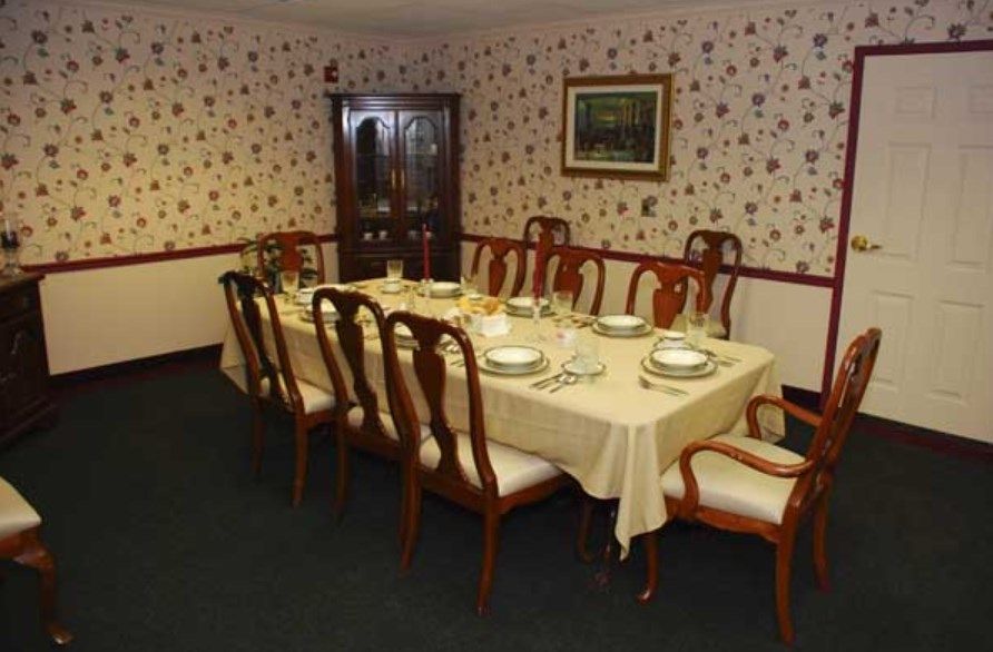 A formal dining room with a table set for a meal, surrounded by wooden chairs and decorated with patterned wallpaper.
