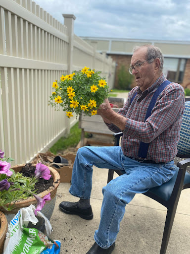 An elderly man carefully arranging a bouquet of vibrant yellow flowers while enjoying the outdoors.