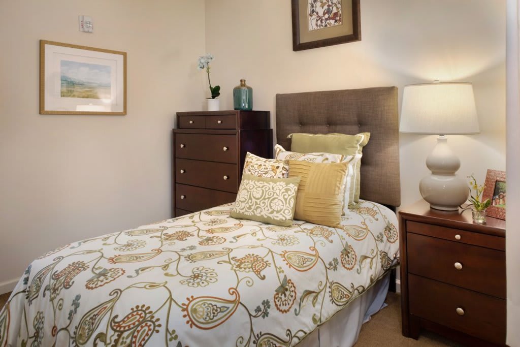A cozy bedroom featuring a single bed with patterned bedding, complemented by a nightstand and dresser.