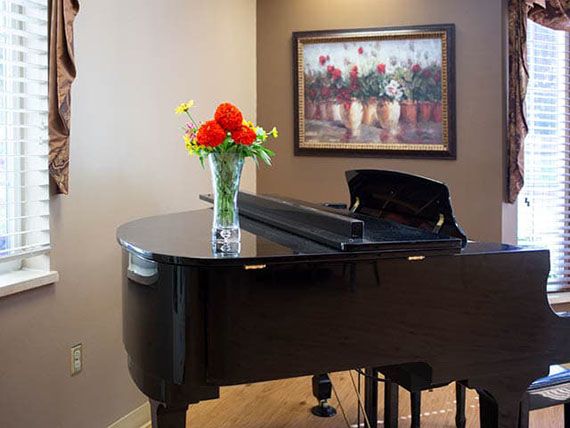 A grand piano with a vase of flowers on top, set in a stylish room with a painting on the wall.