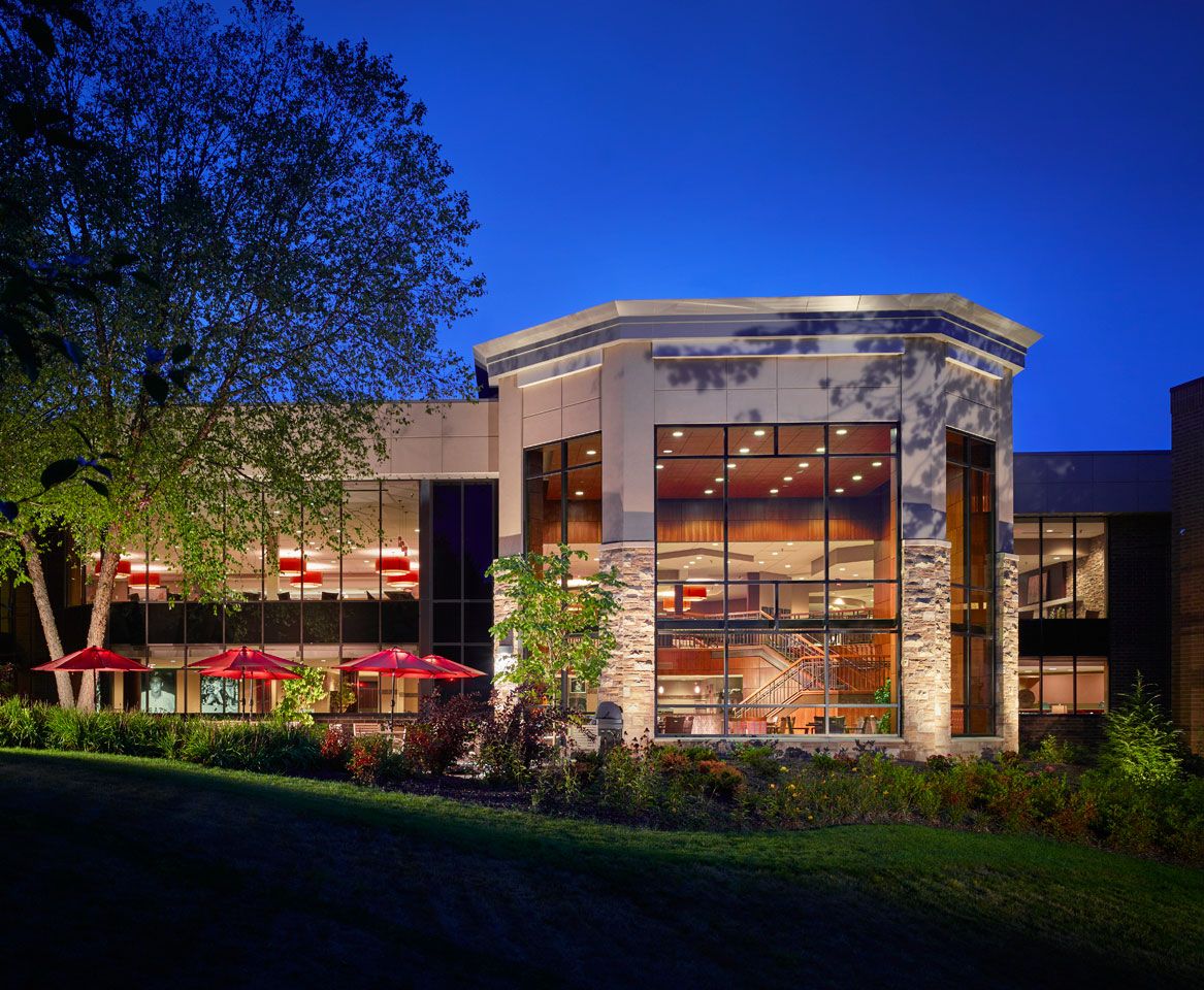 A beautifully lit building at night with surrounding trees and outdoor seating.