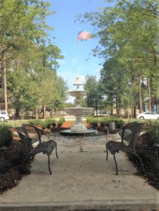 A serene park scene featuring a central fountain lined with benches and surrounded by trees.