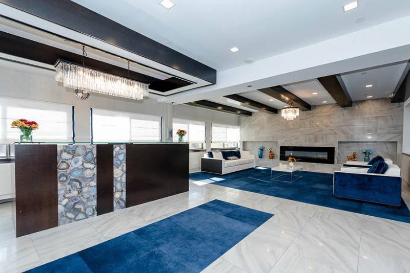 A spacious and luxurious modern living room featuring blue rugs, elegant chandeliers, and sleek ceiling beams.