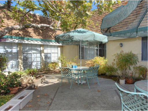 A tranquil outdoor patio perfect for relaxation, featuring a table with an umbrella surrounded by lush greenery.