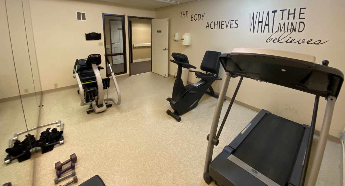 A small fitness room with exercise equipment including a treadmill and stationary bike, featuring a motivational quote on the wall.
