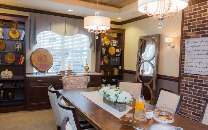 A well-decorated dining room with a wooden table, cushioned chairs, elegant lighting fixtures, and floral centerpiece.