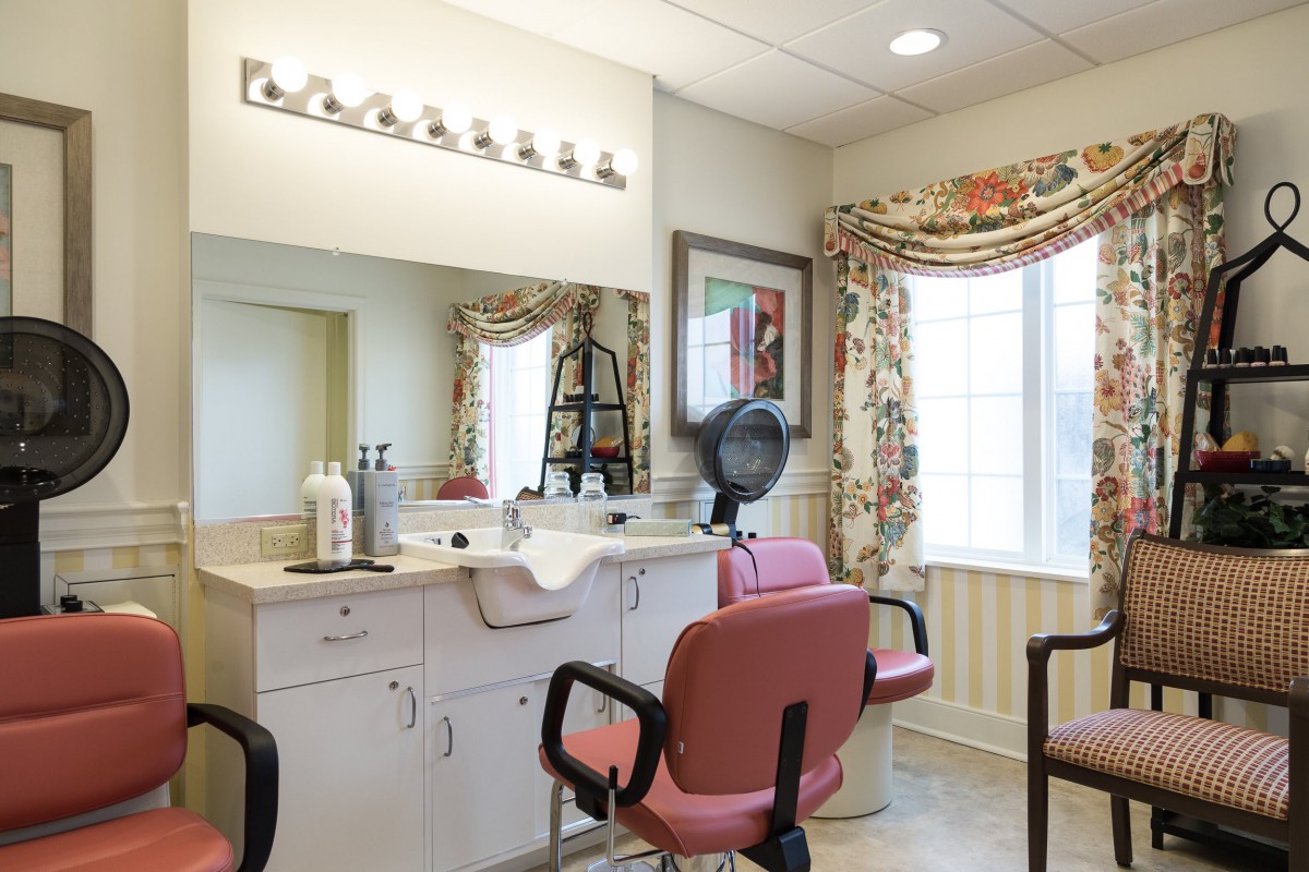 A well-lit hair salon interior with pink chairs, a vanity mirror, and colorful curtains.