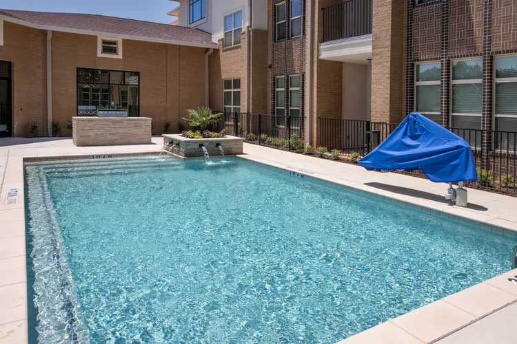 A modern apartment complex featuring an outdoor swimming pool on a sunny day.