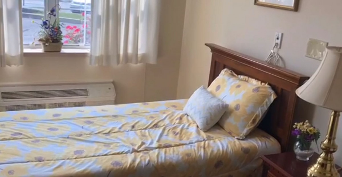 A cozy bedroom with a bed featuring a yellow-patterned comforter and pillows near a window with curtains.