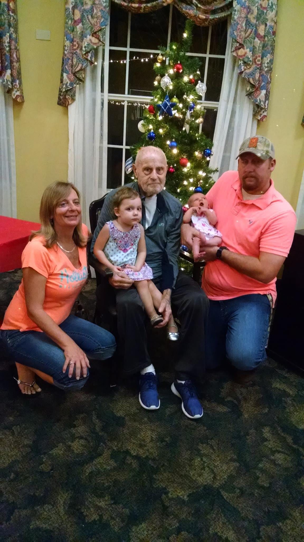 A family gathers around a Christmas tree, smiling for a group photo with young children.