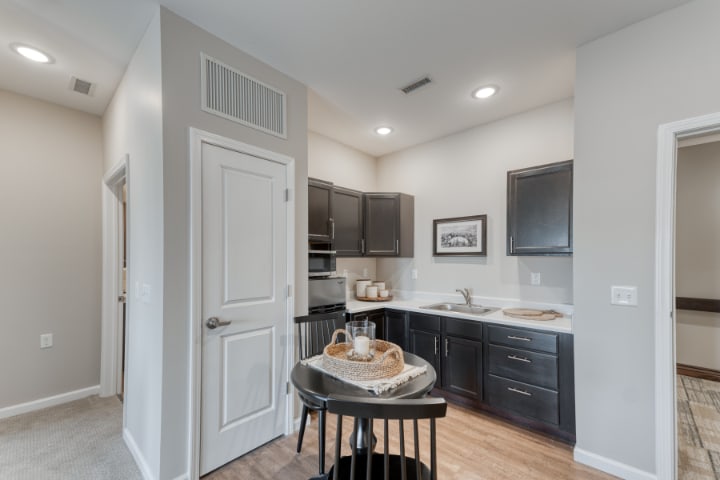 A modern and compact kitchen in an apartment setting with dark cabinets and a small dining table.