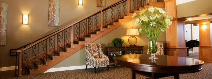 A cozy interior space featuring a staircase with a wooden railing, a floral patterned chair, and a lamp on a table.