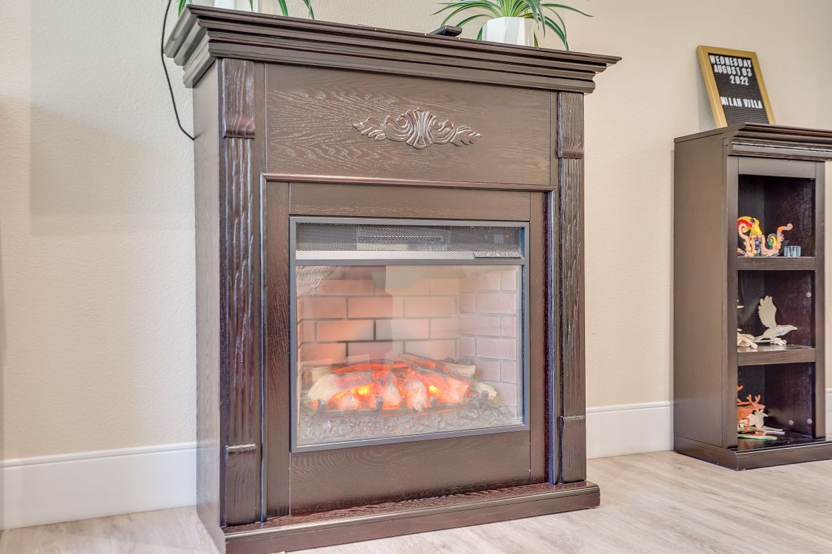 A cozy electric fireplace with a dark wooden frame and decorative engraving, featuring glowing embers inside.