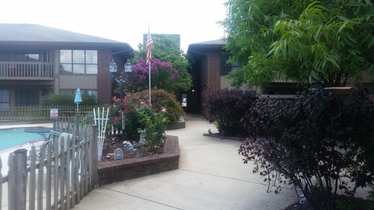 A well-maintained garden pathway leading to a brick building, adorned with vibrant plants and a flag.