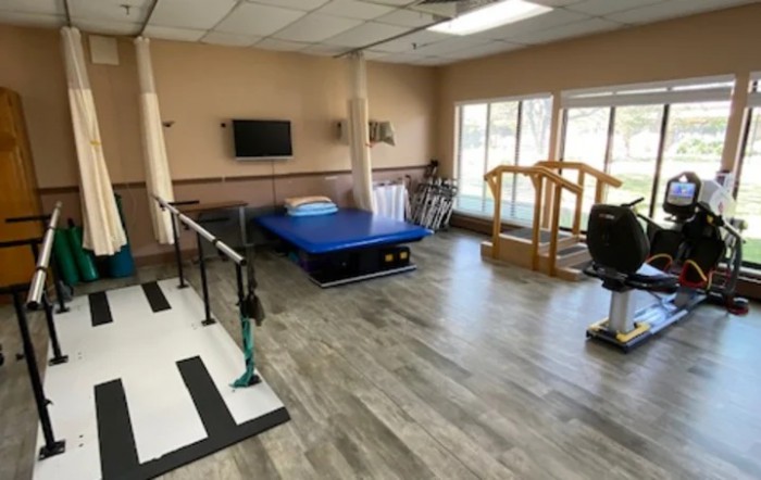 A rehabilitation room equipped with parallel bars, a therapy bed, and other exercise equipment.