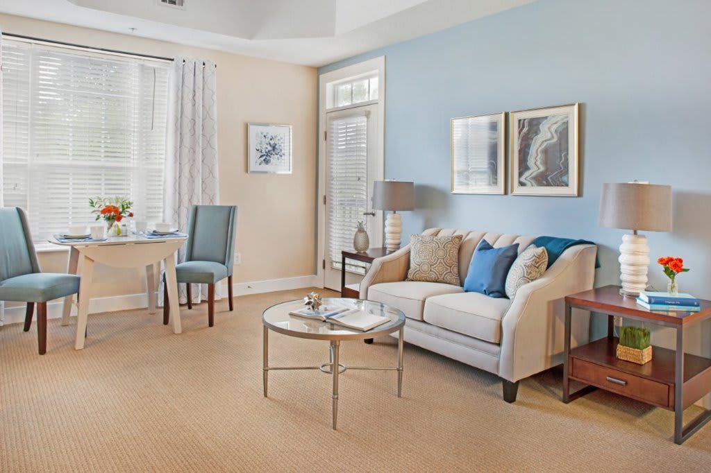 A cozy living room with blue and beige tones, featuring a comfortable sofa, decorative pillows, a round coffee table, and framed artwork on the walls.