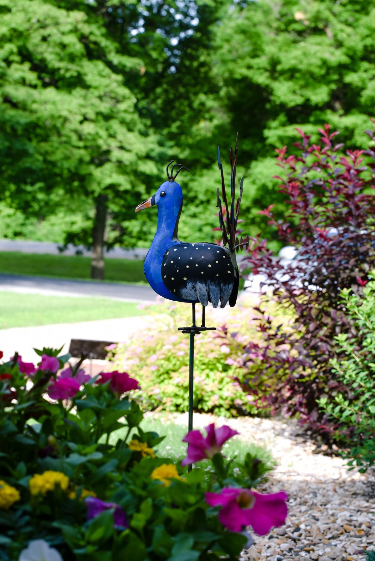 A colorful metal bird sculpture stands amidst a vibrant garden.