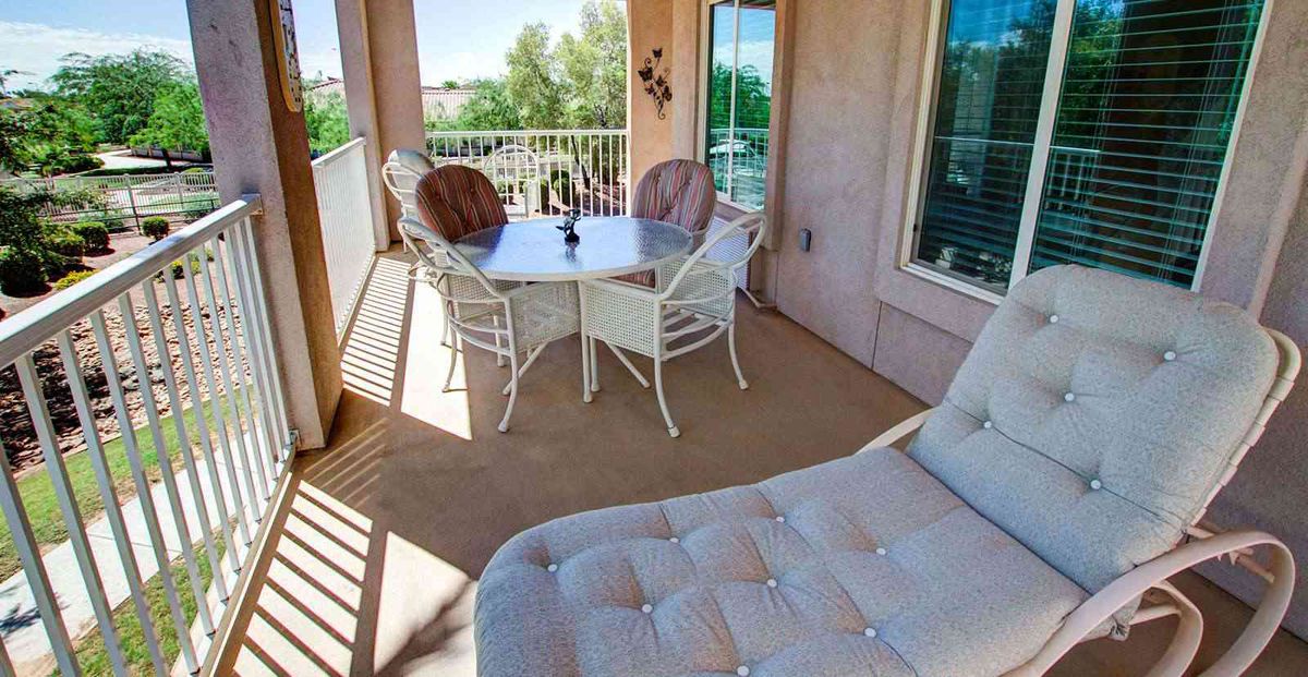 A sunny balcony with a table, chairs, and a comfortable lounger.