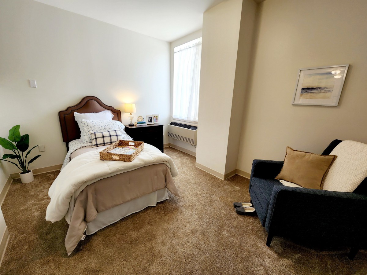 A cozy bedroom with a single bed, nightstand, and a comfortable chair.